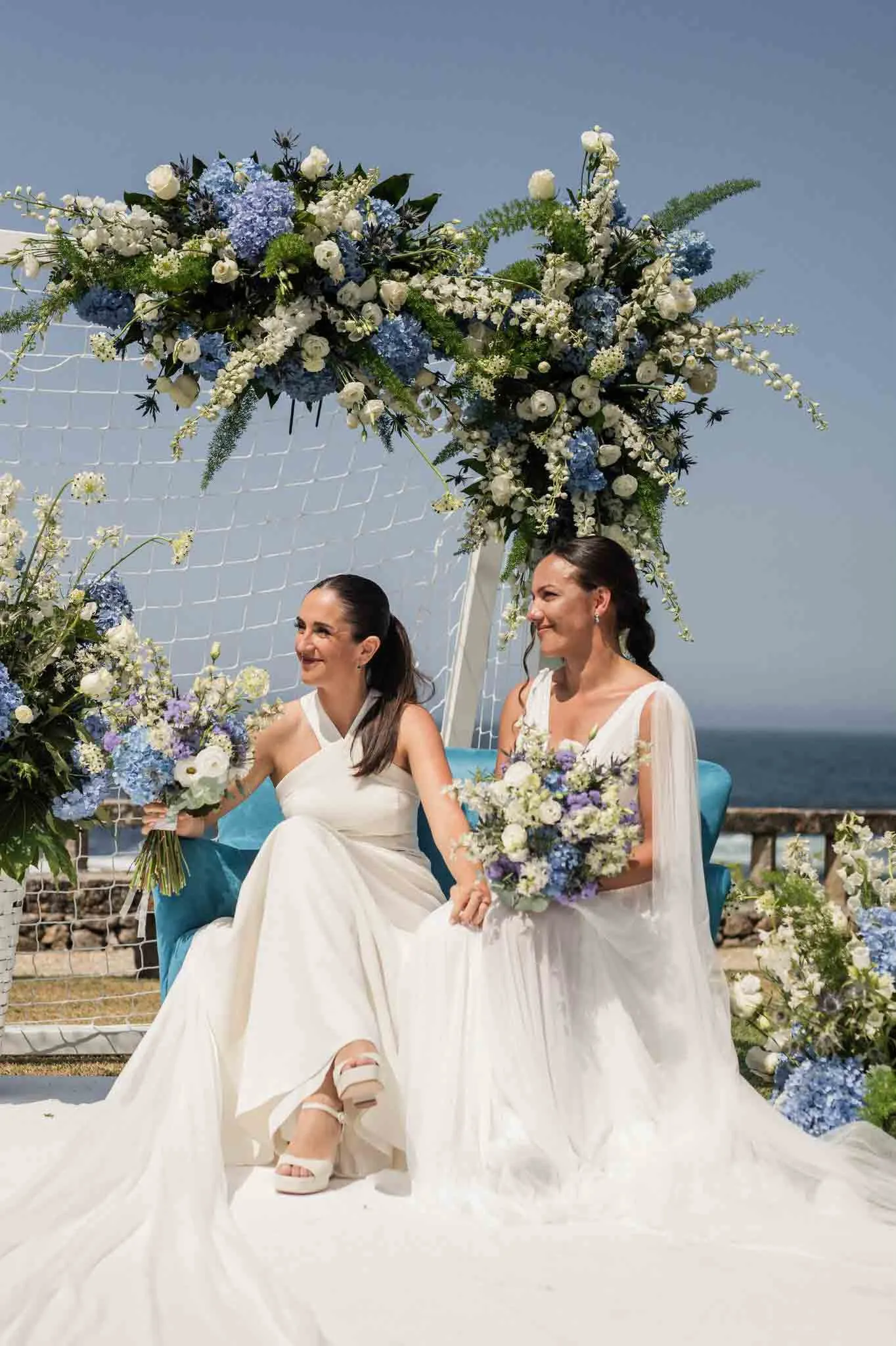 Novia e invitada compartiendo la celebración bajo flores azules y blancas